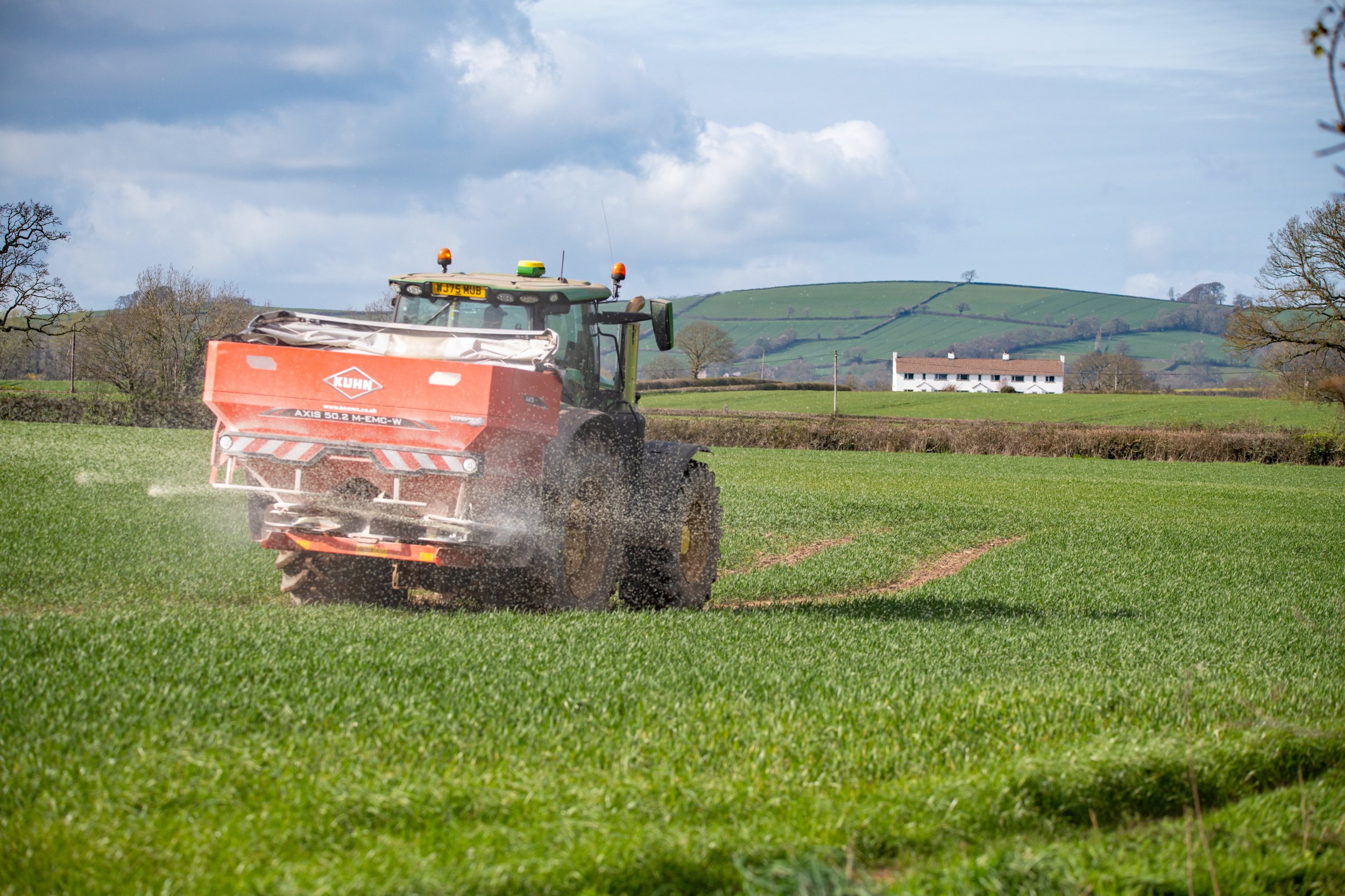 A tractor with a fertiliser spreader working in a green field.