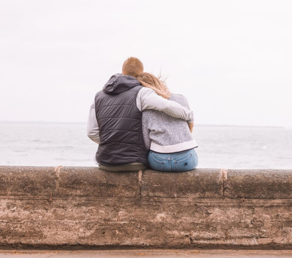 couple hugging on wall next to sea